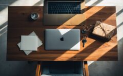 Aufsicht auf einen Schreibtisch mit Laptop, Schlüssel und Aktenordnern im gedeckten Tageslicht