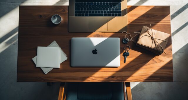 Aufsicht auf einen Schreibtisch mit Laptop, Schlüssel und Aktenordnern im gedeckten Tageslicht